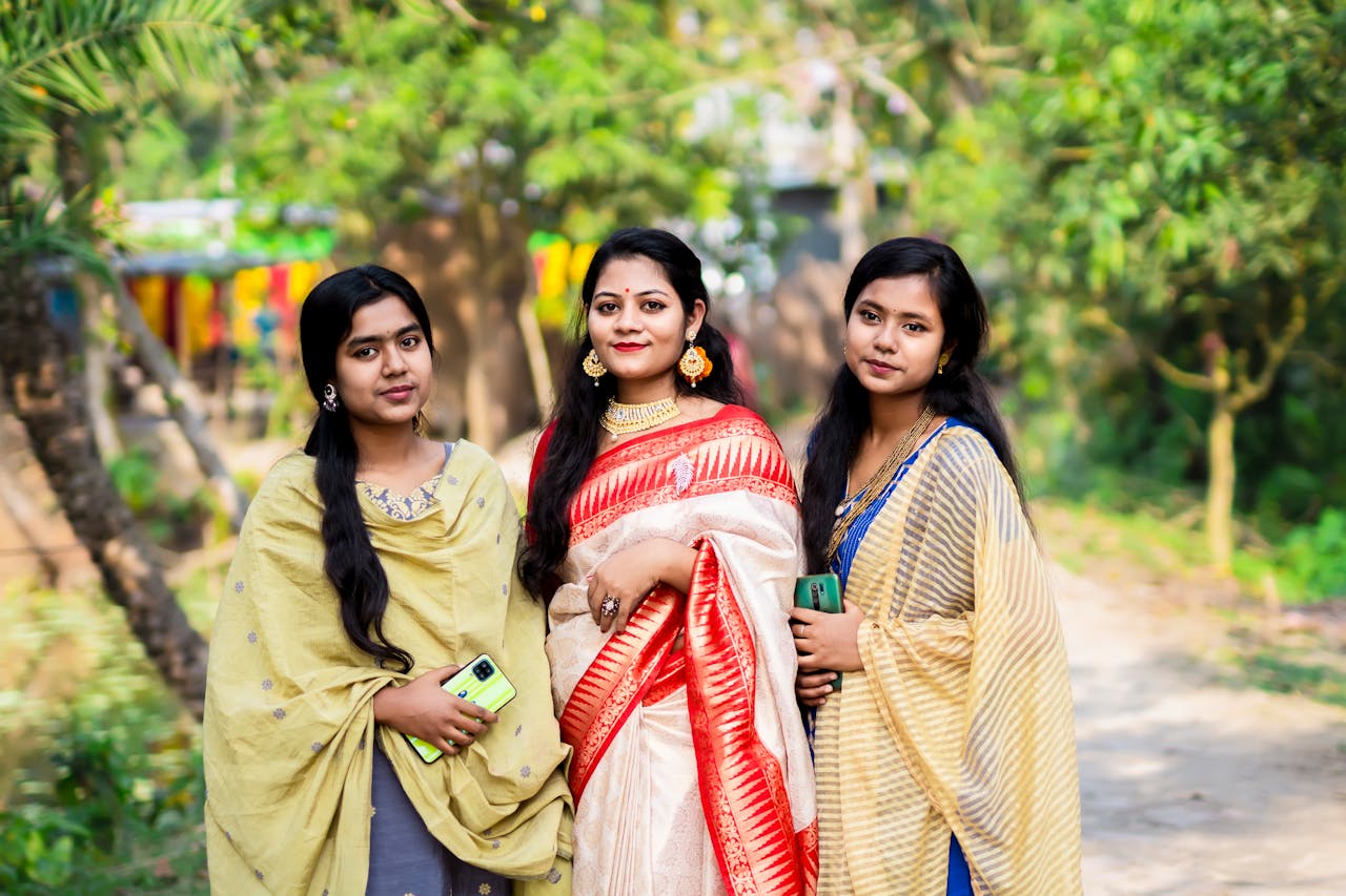Three women posing outdoors in colorful Indian saris, displaying traditional fashion and friendship.