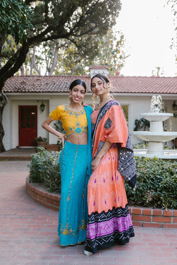 Two women in colorful traditional clothing posing outdoors near a fountain.