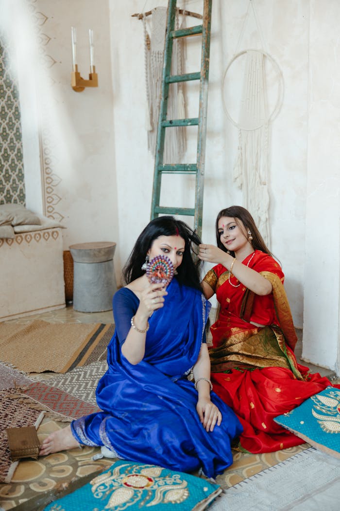 Two women in saris engaging in traditional ritual with cultural decor.