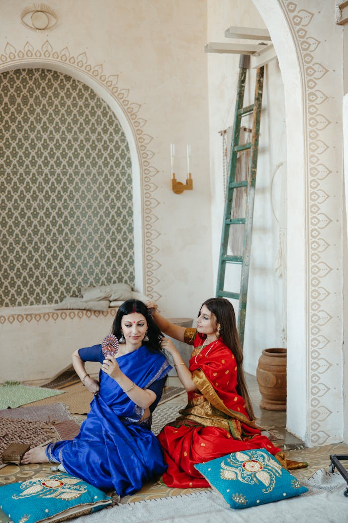 Two women in elegant traditional Indian sarees in a vintage styled room.